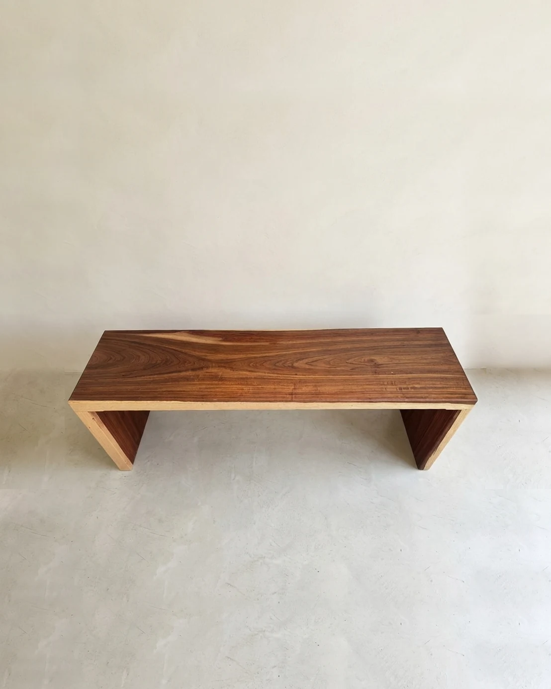 A solid kiaat waterfall bench, the grain running unbroken over the edge into the legs, with pale sapwood along the edges