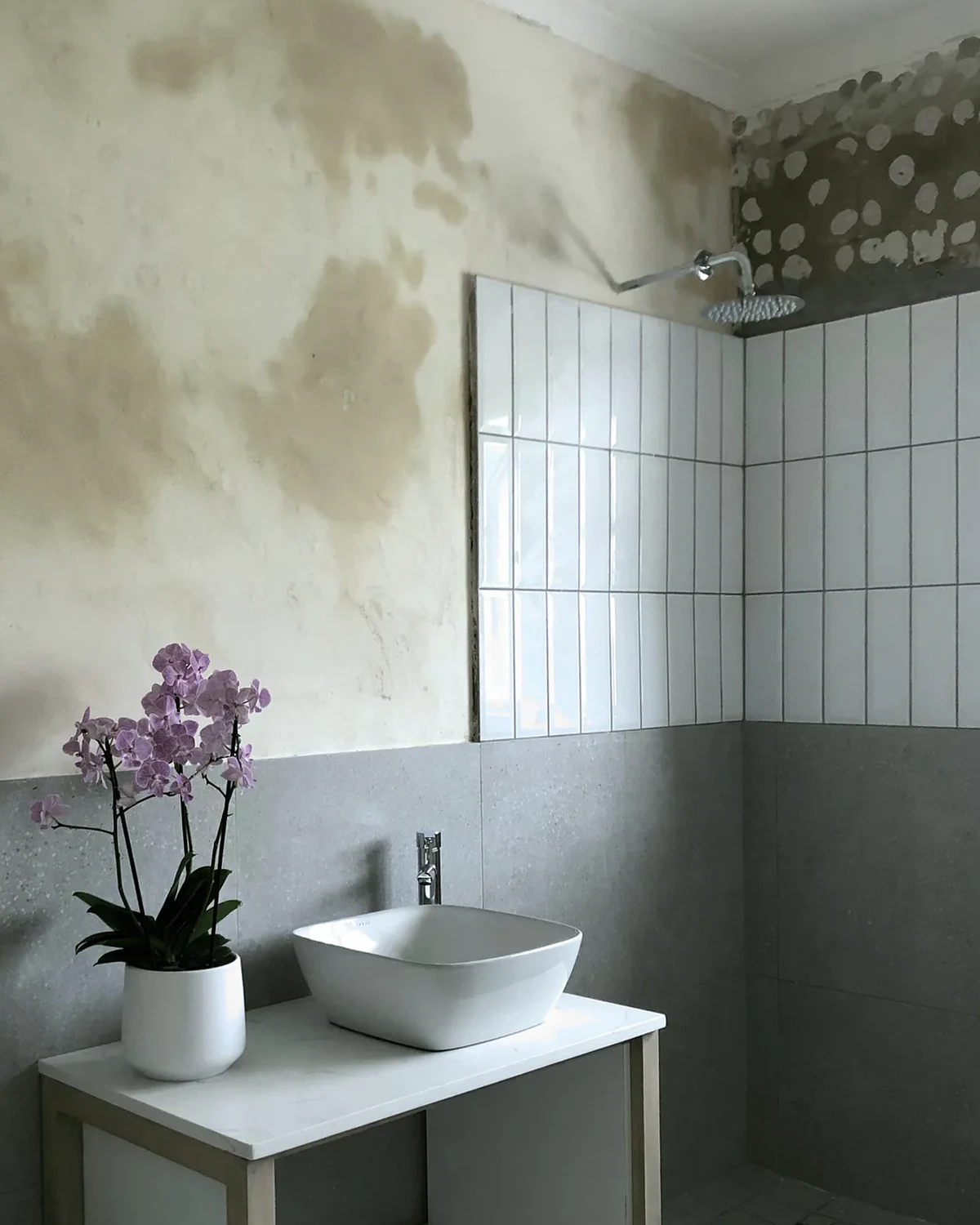 A bathroom renovation in progress, with new shower tiles and fittings beside a wall awaiting its final skim